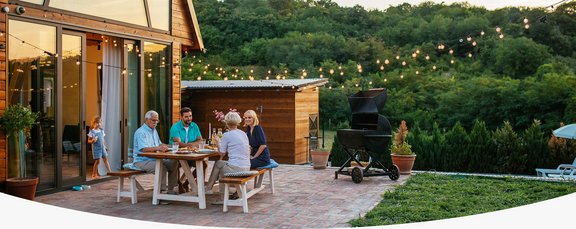 Familie sitzt abends auf der Terrasse bei Essen und Lichterkette