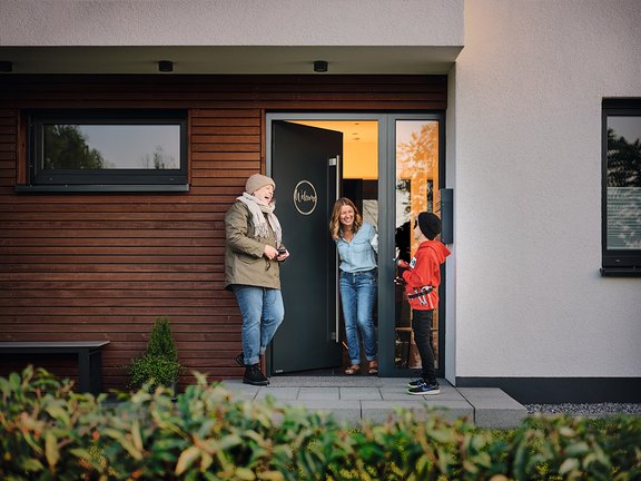 Familie begrüßt sich herzlich an der Haustür eines modernen Hauses mit Holzverkleidung