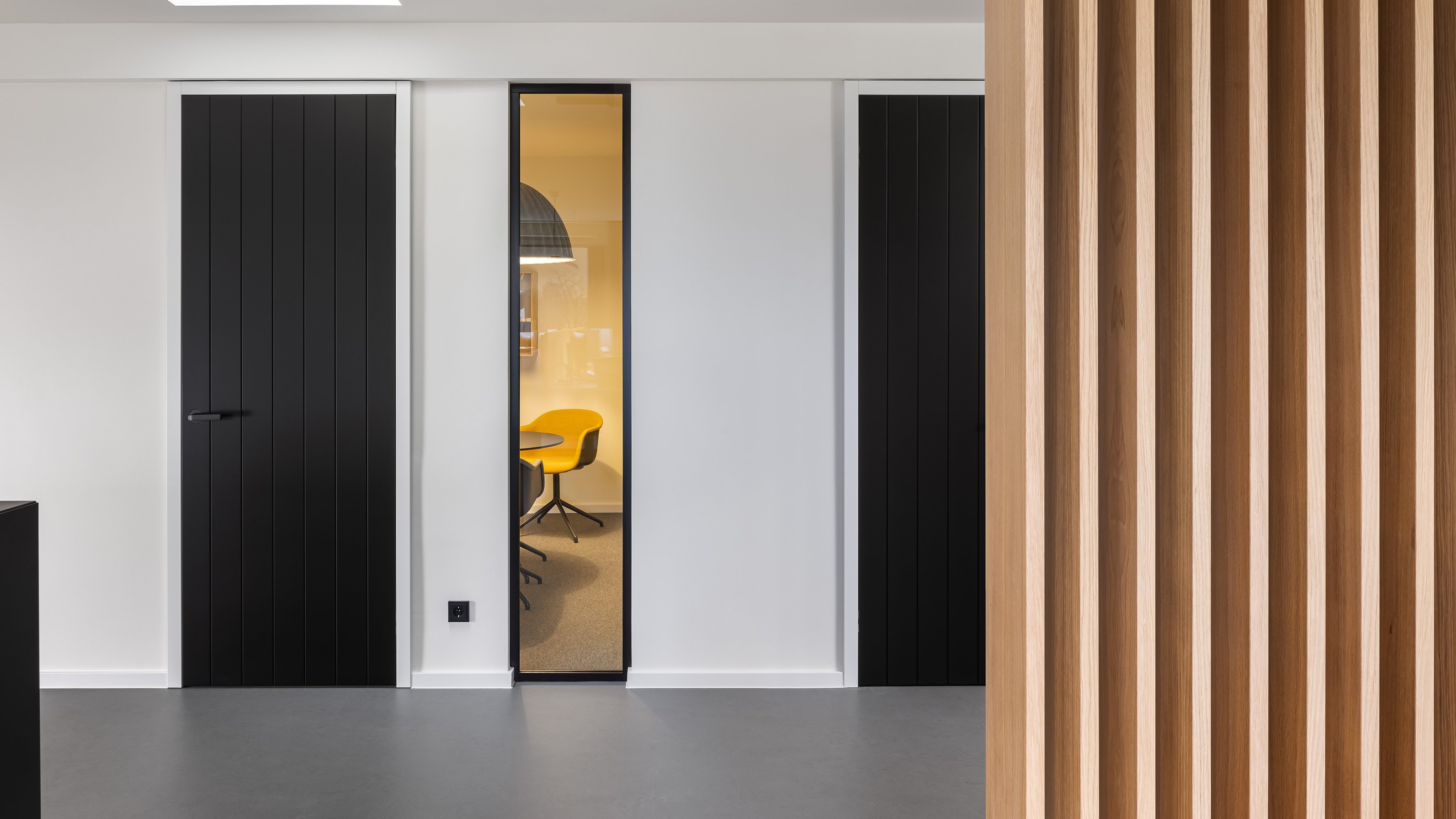 Schwarze Innentüren mit vertikaler Linienstruktur in einem modernen Büro mit gelbem Konferenzstuhl
