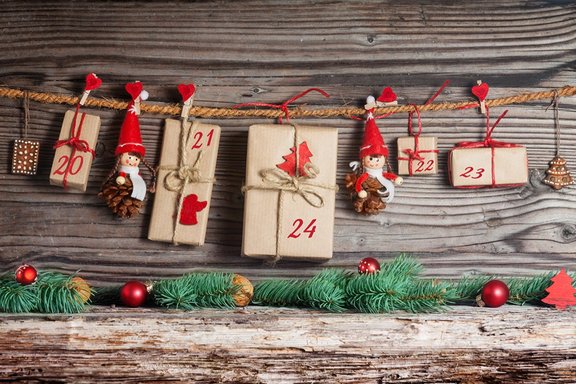 Rustikaler Adventskalender mit nummerierten Päckchen, Weihnachtsfiguren und Tannendeko vor Holzplanken