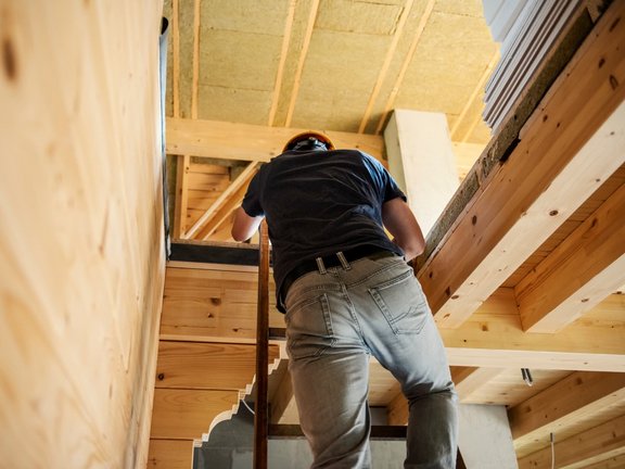 Handwerker steigt über eine Leiter in ein ausgebautes Dachgeschoss mit sichtbarer Dämmung und Holzverkleidung