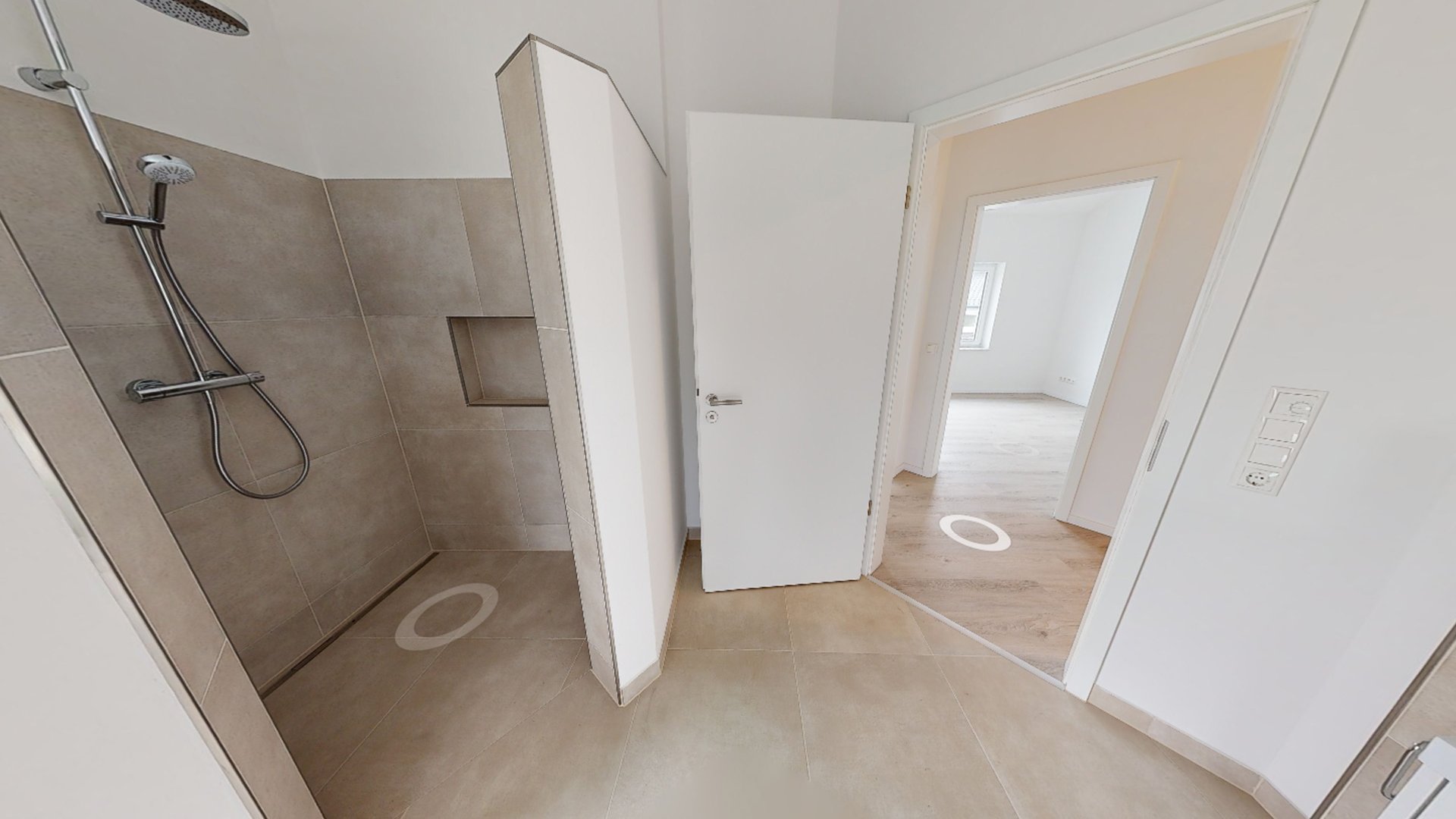 Moderne geflieste Dusche mit Regendusche, halbhoher Trennwand und angrenzender Tür in einer Neubauwohnung