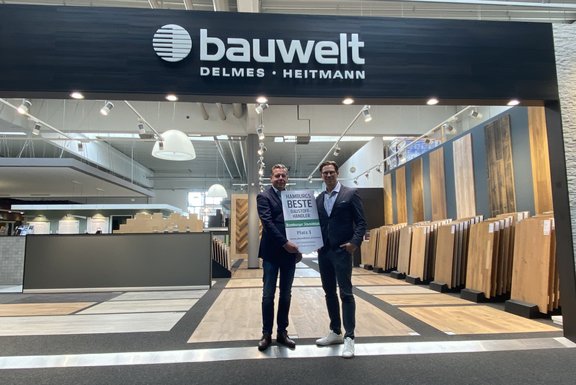 Zwei Männer in der bauwelt-Ausstellung mit Parkett Fußböden, halten eine Auszeichnung für „Hamburgs beste Baustoffhändler"