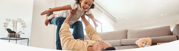 Vater spielt mit Tochter im modernen Wohnzimmer auf einem Teppichboden, Spielzeug und Kuscheltiere liegen auf dem Boden