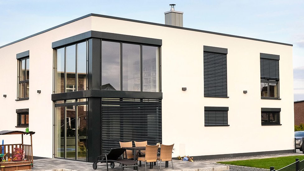 Zweistöckiges Flachdachhaus mit weißer Putzfassade und schwarzen Fensterläden