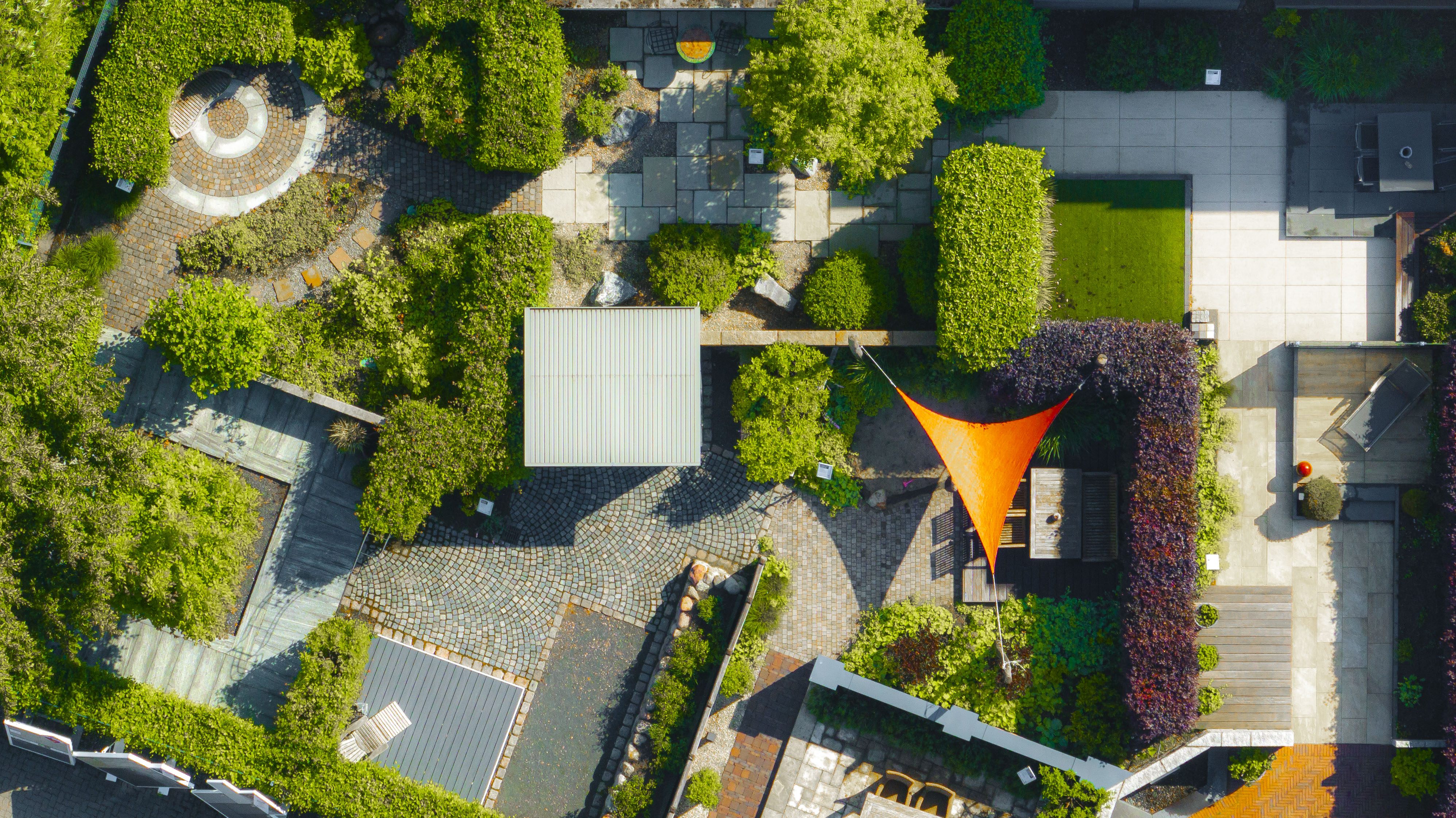 Luftaufnahme der detaillierten Gartenausstellung bei Bauwelt Buchholz mit verschiedenen Pflasterflächen, Sitzgelegenheiten, Pflanzen und Mustern.