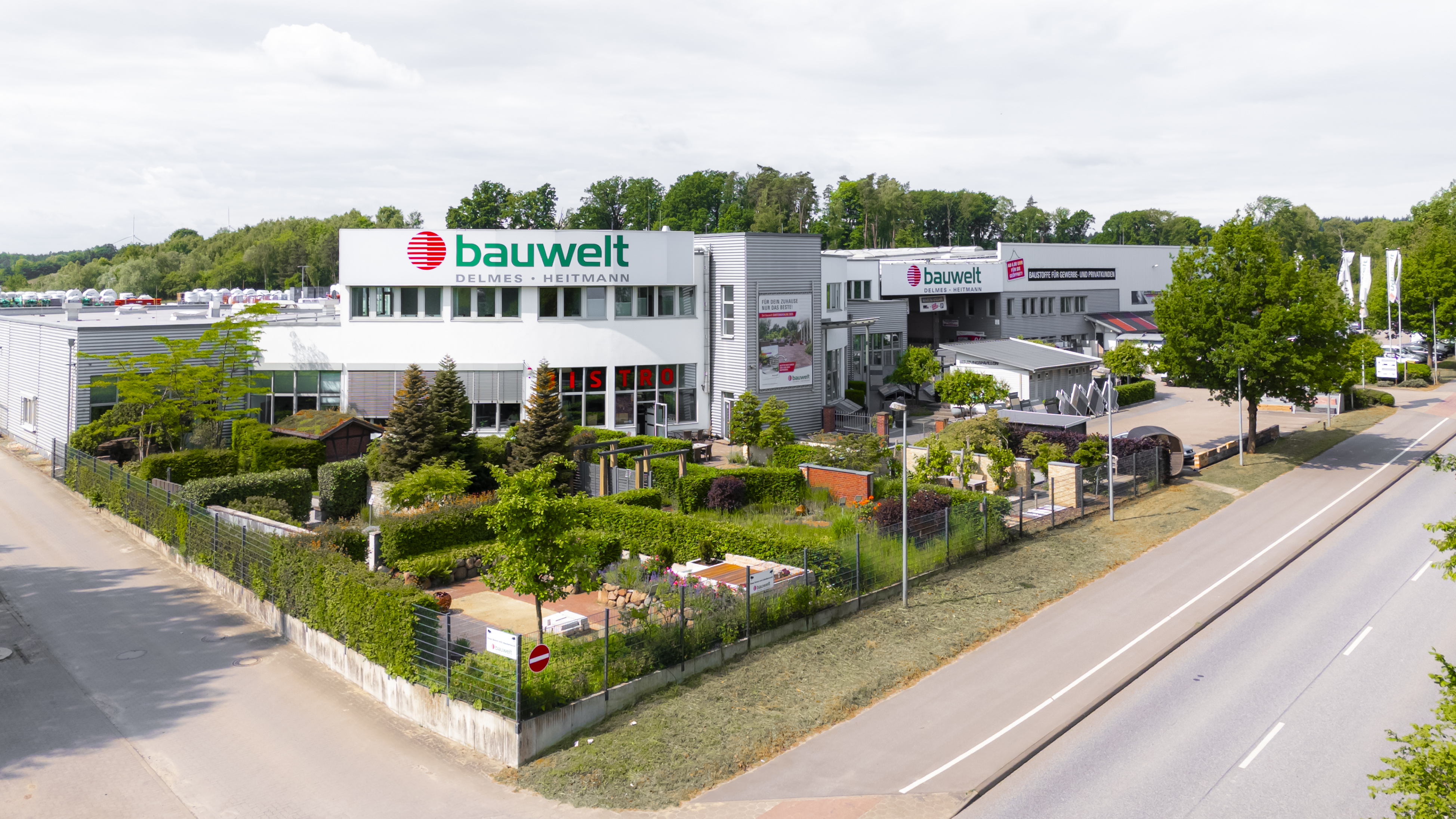 Ansicht des Haupteingangs der bauwelt mit gepflegter Gartenanlage und moderner Architektur an einer Straße.