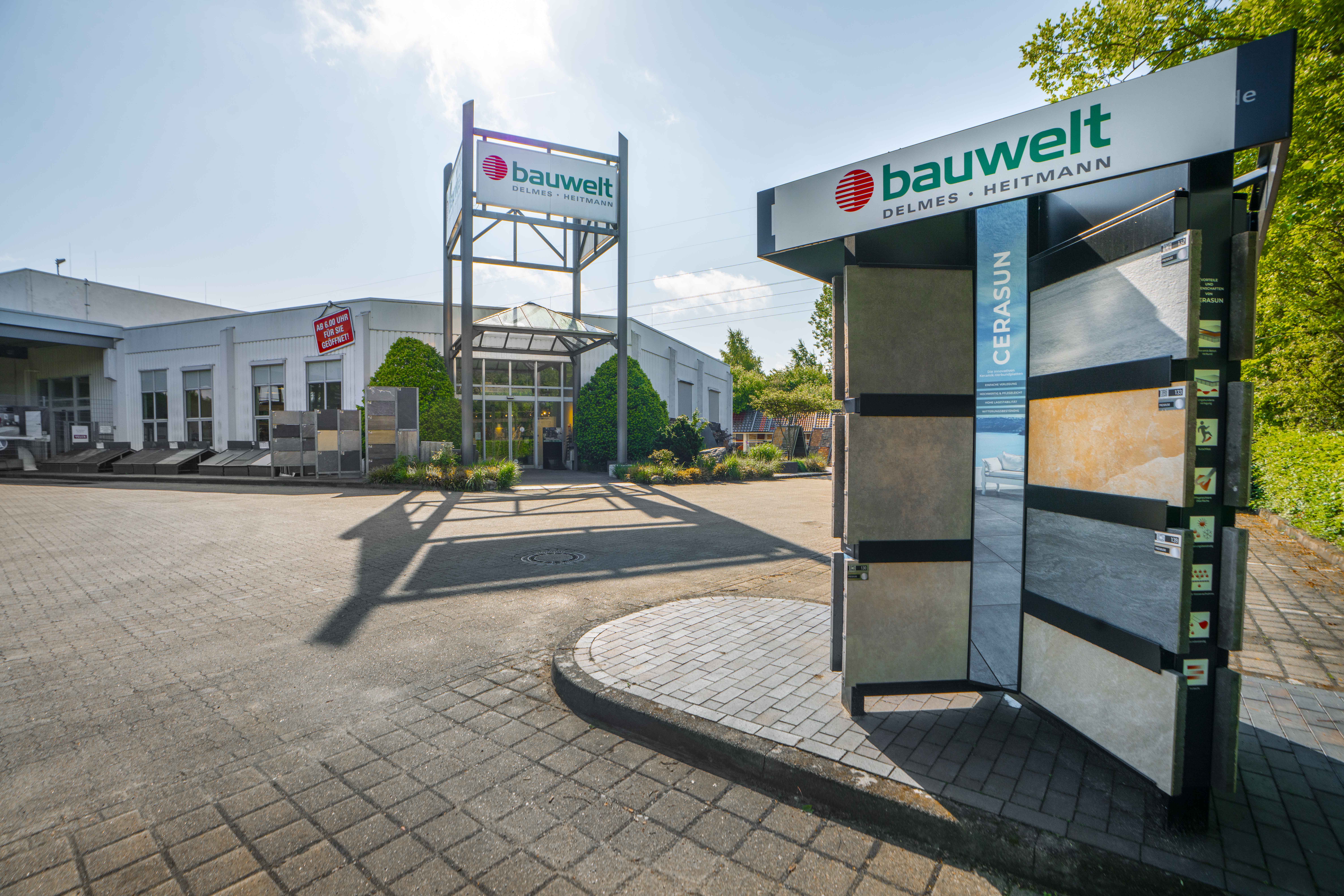 Außenansicht des Bauwelt-Standorts Buchholz mit großer Garten- und Musterausstellung sowie angrenzender Lagerhalle, umgeben von viel Grün.