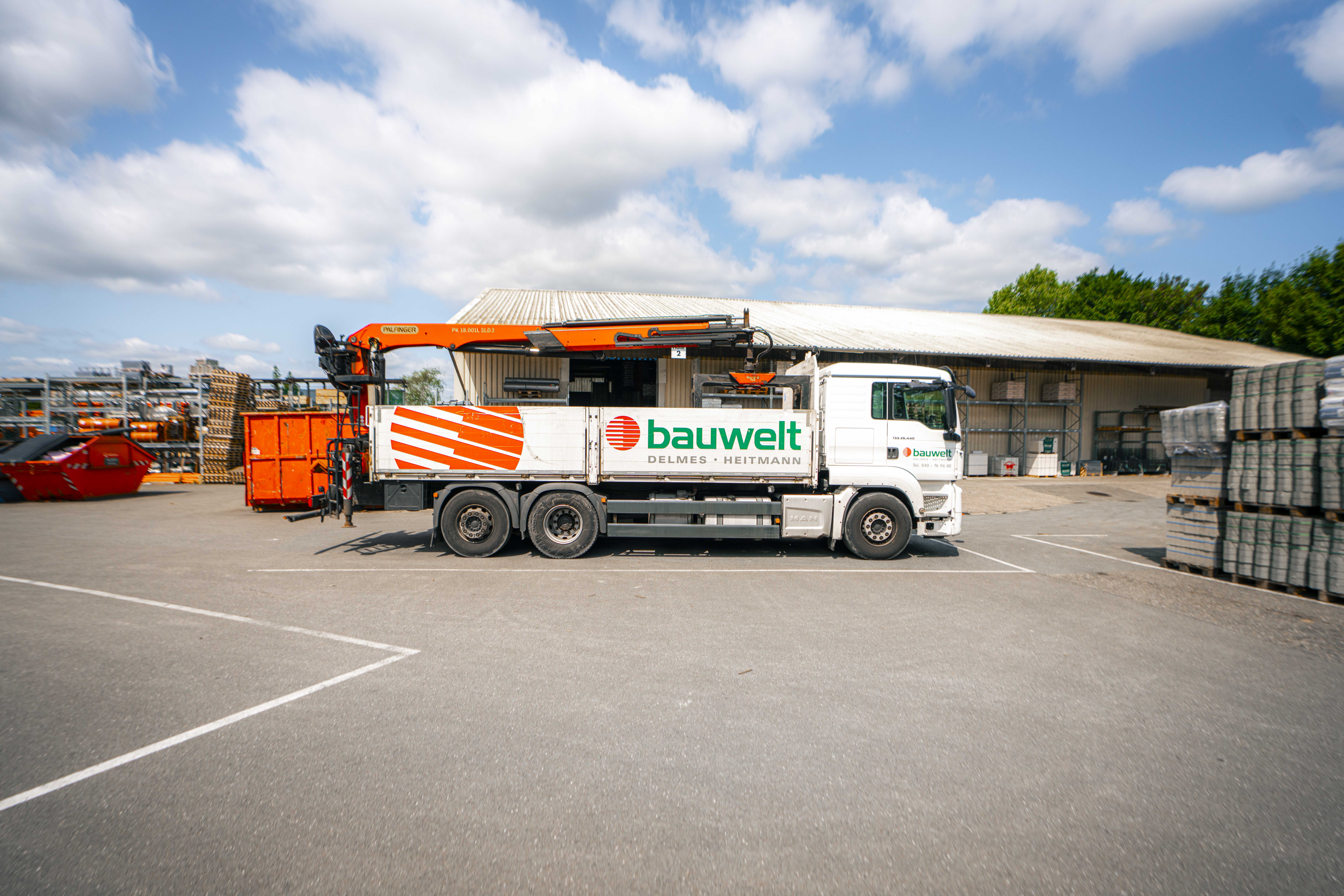 LKW mit Bauwelt-Branding auf dem Lagerhof in Glinde, umgeben von Baustoffpaletten und Containern.