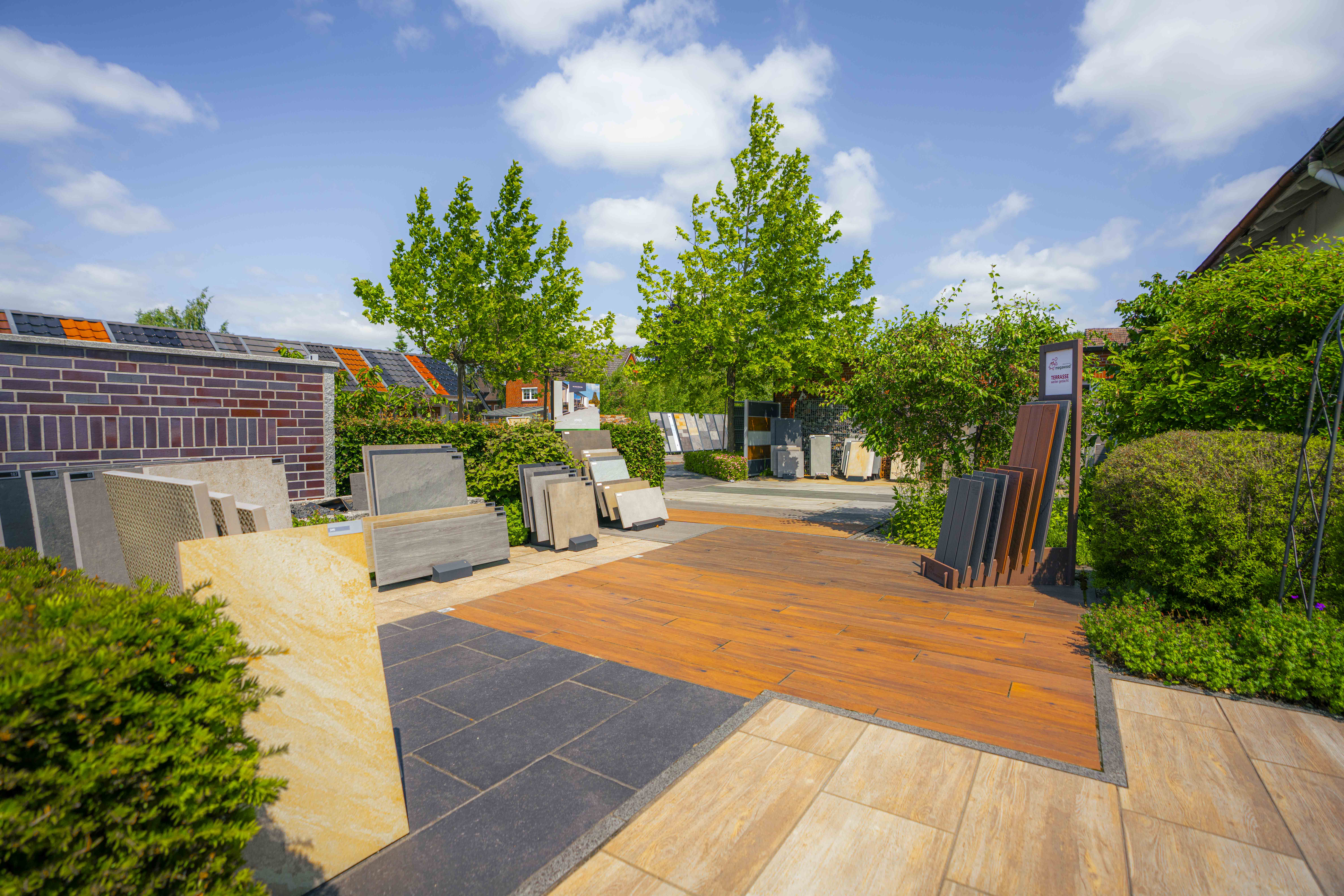 Außenaufnahme im Mustergarten Kirchwerder mit großformatigen Plattenmustern, Terrassendielen und Baumkulisse im Hintergrund.