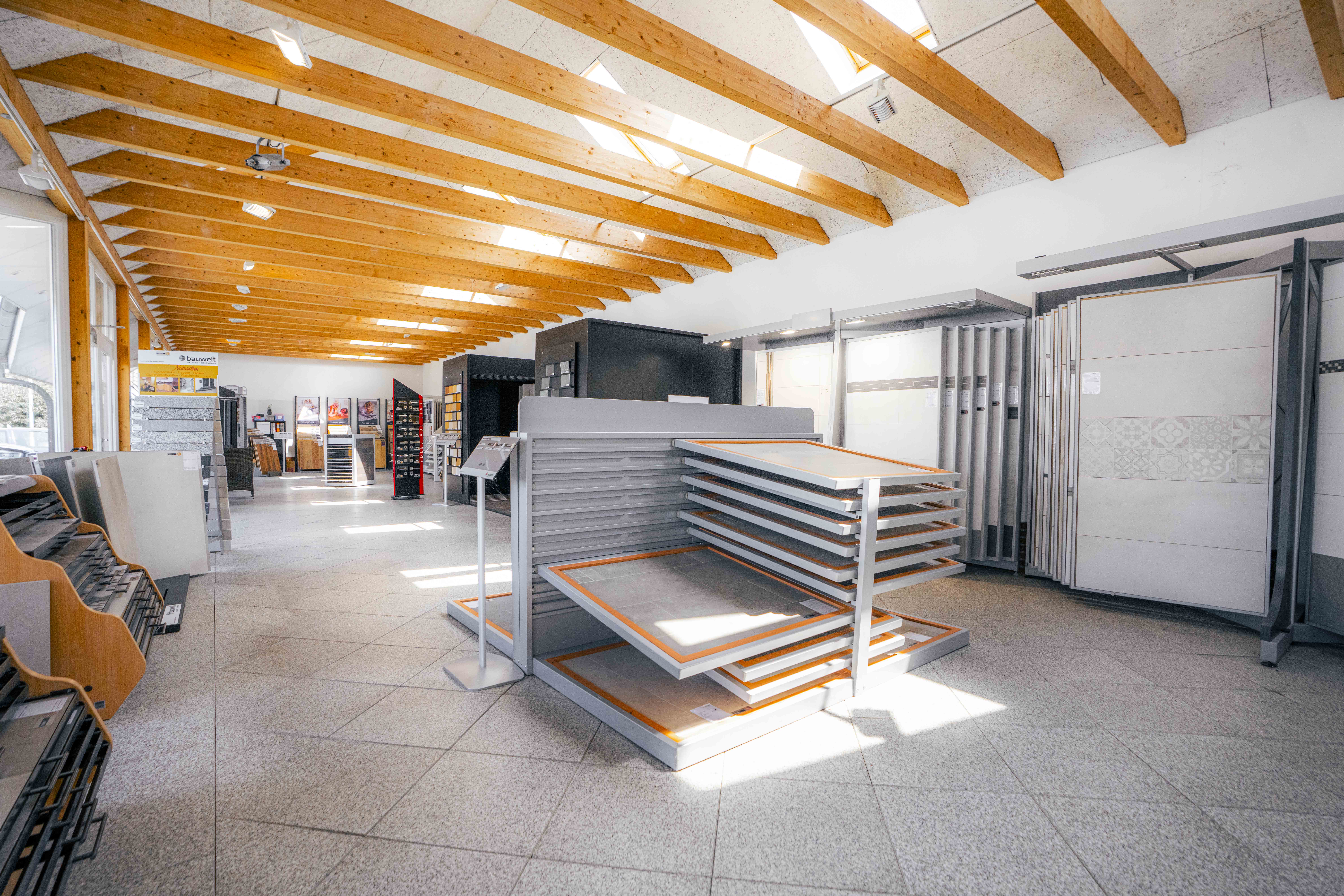 Innenaufnahme der Bauwelt-Ausstellung in Kirchwerder mit großflächigen Fliesenmustern, natürlicher Beleuchtung und Holzbalkendecke.